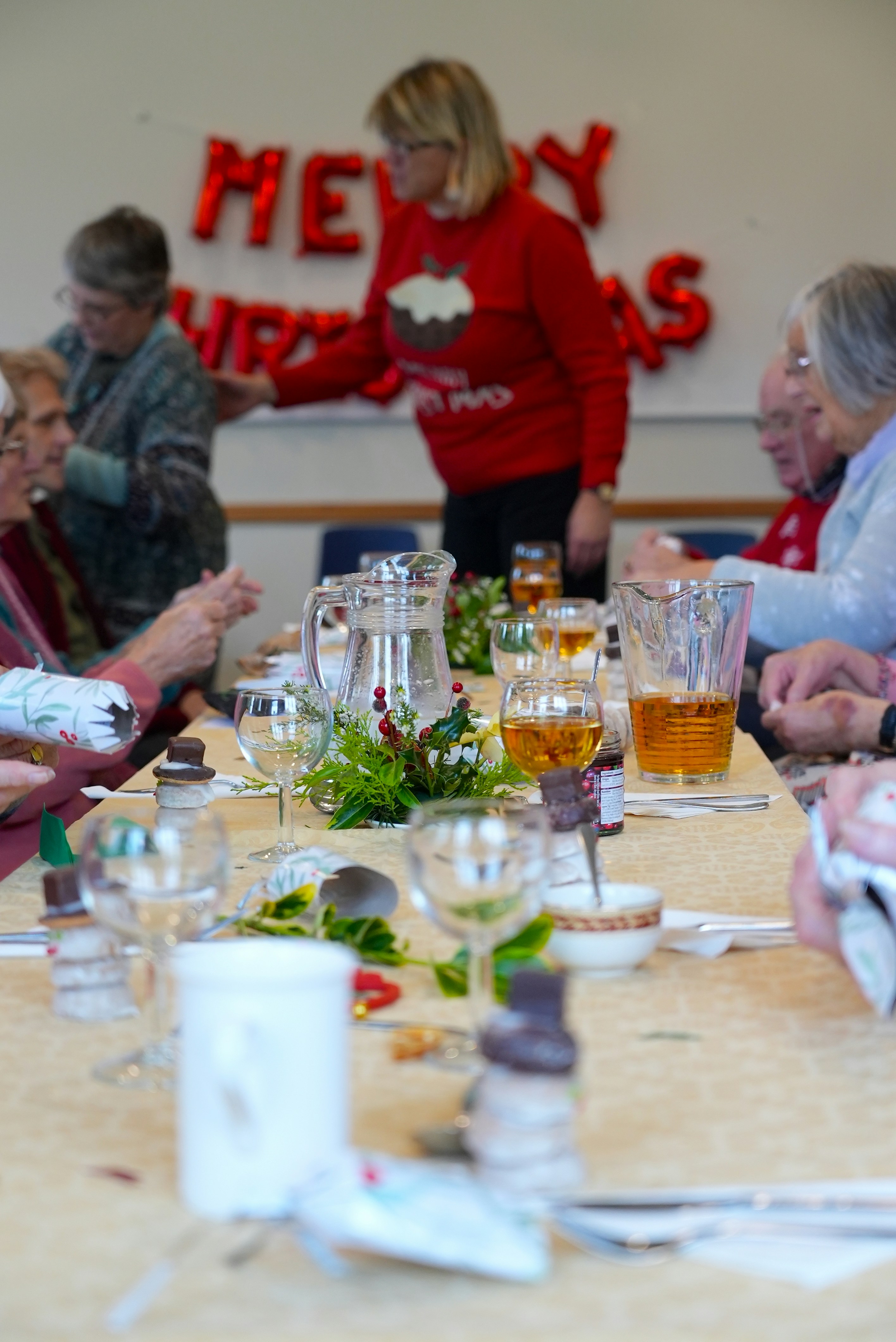 Table of a christmas community dinner with decorations and drinks glasses on it, people in the background